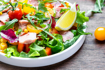 Fresh tuna and vegetable salad with cherry tomatoes, onion, sweet corn, paprika, lettuce, radicchio and arugula. Rustic wood table background, top view