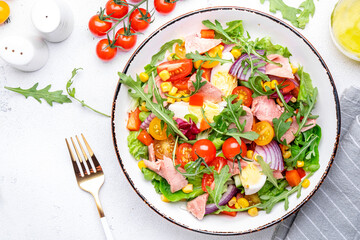 Fresh tuna and vegetable salad bowl with cherry tomatoes, onion, sweet corn, red paprika, lettuce and arugula. White  table background, top view
