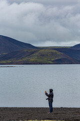 Fototapeta na wymiar Unrecognizable young female tourist taking photos with her phone, lake, Southern Iceland