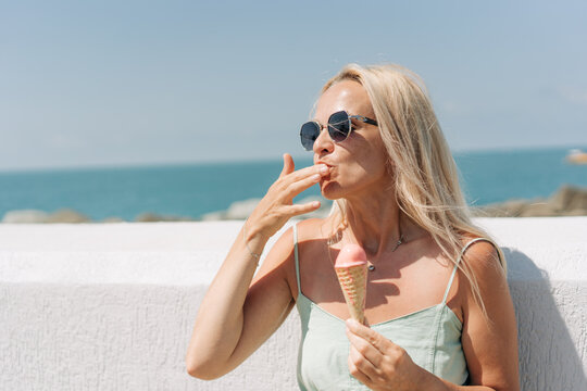 A woman eats melting ice cream and licks her fingers on a hot summer day.