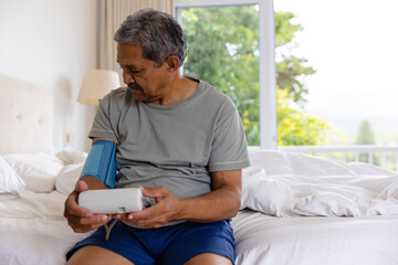 Biracial senior man taking blood pressure in bed at home - Powered by Adobe