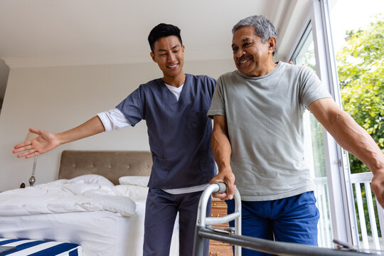 Happy diverse male doctor advising and senior male patient using crutches at home