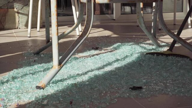 Sweeping broom moving broken glass to pile on floor closeup. Close-up cleaning wracked table leftovers in sunshine on terrace