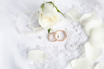festive wedding background. Two gold wedding rings among white rose petals on satin fabric and lace tulle. Top view.