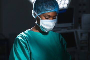 Fototapeta na wymiar African american female surgeon wearing surgical gown and face mask in operating theatre