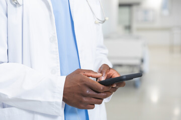 Midsection of african american male doctor using smartphone in corridor at hospital