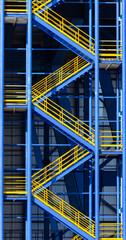 Metal construction fire escape ladder with blue and yellow . .Escape staircase. Fire escape route of a factory. Fire escape stair building. Fire escape staircase on the exterior wall of a warehouse