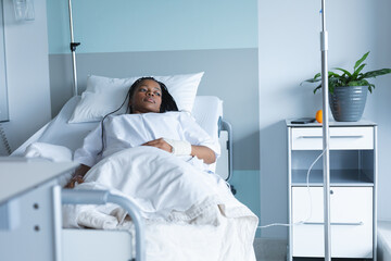 African american female patient lying on bed and looking away in hospital room