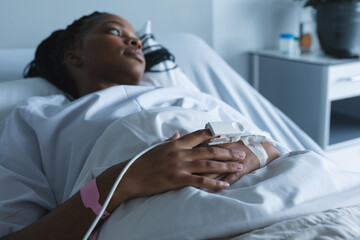 African american female patient with pulse oximeter on hand, lying on bed in hospital room