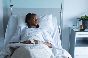 African american female patient looking away, lying on bed in hospital room