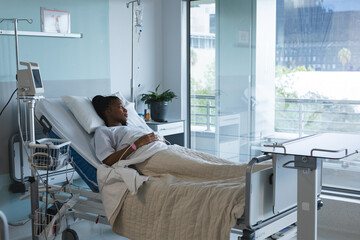 African american female patient looking away, lying on bed in hospital room