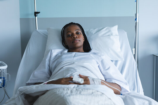 Portrait of african american female patient with braids, lying in bed at hospital