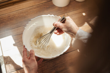 Girl whipping dough for baking bread. Close up of a wife cooking in kitchen, using whisk to stir different ingredients for liquid dough