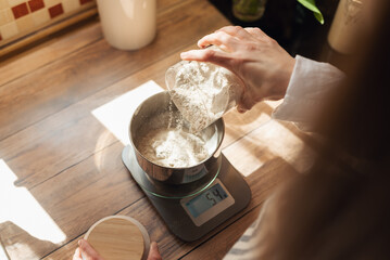 Measuring flour with electronic kitchen scales for cooking something. Girl pouring flour to the...