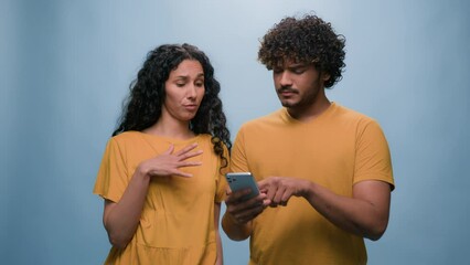 Multiracial couple Indian man Hispanic woman shopping online mobile phone store choosing goods in internet shop booking order thumb up ok goals purchase combined family budget blue studio background