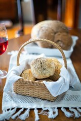 Basket full of tasty buns over and a glass of red wine on a wooden table