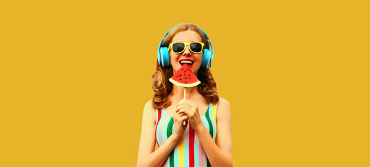 Summer colorful portrait of cheerful happy smiling young woman model posing in headphones listening to music with juicy slice of watermelon on yellow background