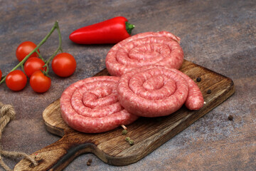 Bratwurstschnecken auf einem Holzbrett mit Tomaten und Paprika.