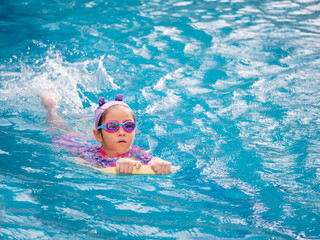Fototapeta na wymiar Asian child or kid girl wearing swimming suit to learning on swimming pool , learn and training swim on kick board