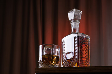 a glass of whiskey or rum with ice and a carafe of whiskey or rum on a dark black background