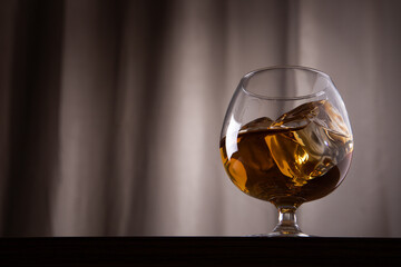 a glass of whiskey and ice on a wooden table on a dark background