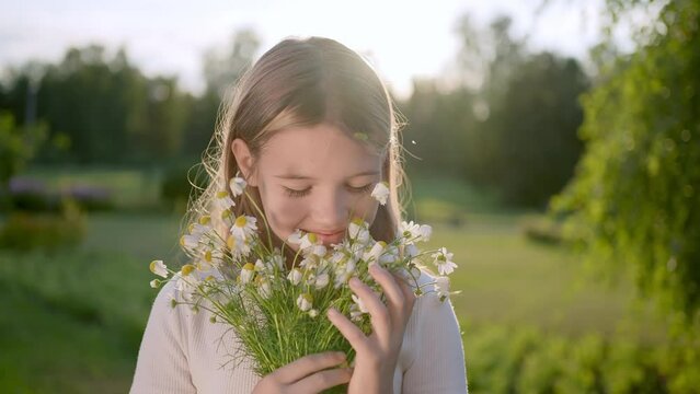 Portrait of happy little beautiful smiling cute girl child sniffing chamomile bouquet at meadow sunny day summer sunset park looking at camera. Kid having fun, Happy family field. Children Childhood 