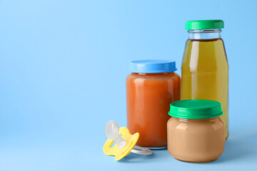 Healthy baby food, juice and pacifier on light blue background, space for text