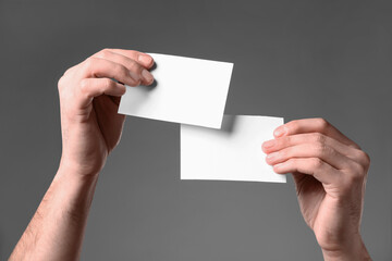 Man holding paper cards on grey background, closeup. Mockup for design