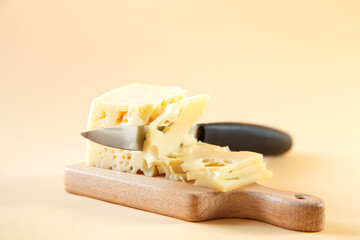 The knife is cutting a piece of cheese with holes on a wooden board.