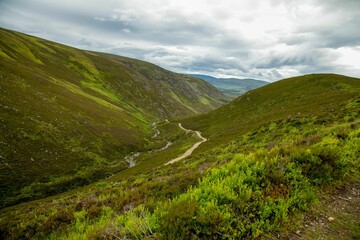 Naklejka premium Serene and picturesque valley framed by a lush blanket of trees and grass, with a cloudy sky