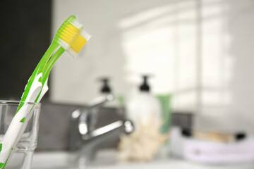 Fototapeta na wymiar Light green toothbrushes in glass holder indoors, space for text