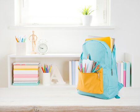 Full school backpack with different colorful stationery on wooden table