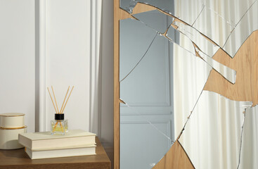 Broken mirror, reed diffuser and books on wooden table in room
