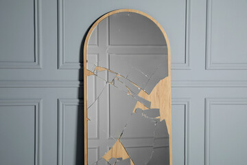 Broken mirror with many cracks near grey wall