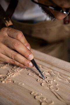 An old Chinese carpenter is carving words on a wooden board, traditional technique, indoor shooting, partial close-up(Translation: The carved text reads "laobanzhang")