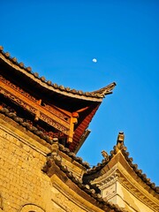 Close-up shot of an ancient tiled roof of a building against a deep blue sky backdrop with the moon
