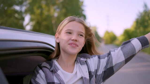 Happy smiling girl sticking heads out car window. Happy girl in car window having fun. Have happy family trip. Cute little child kid girl smiles at wind in car window. Family dream summer trip travel