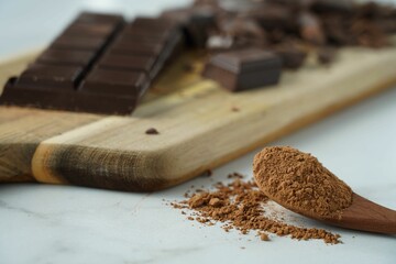 a wooden spoon is filled with brown chocolate powder and a couple dark squares of chocolate