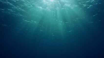 View of sun light from blue abyss, slow motion. Light filters down through blue water. Underwater sun rays in depth ocean. Underwater sun light shine under deep water with ripples on waves surface