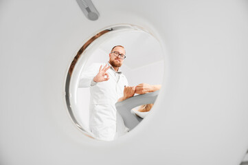 Medical computed tomography or MRI scanner. Male radiologist examine female patient, showing ok...