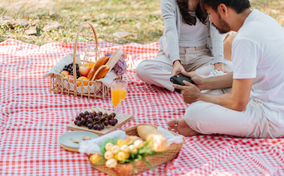 Happy asian couple travel. Woman taking photo of his boyfriend picnic time in park holidays vacation.