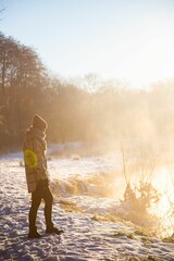 Fototapeta premium a female standing in the snow near a lake in the winter