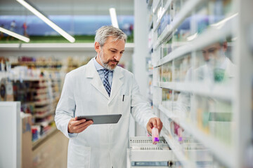 A senior male pharmacist using a digital tablet for medical inventory in a pharmacy.