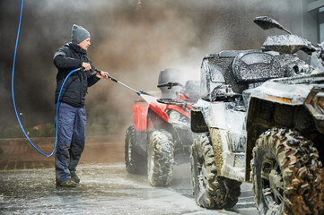 Man cleaning all-terrain vehicle with high pressure water sprayer at self-service car washing...
