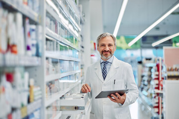 Naklejka na ściany i meble Portrait of a grey-bearded smiling male pharmacy employee with a tablet.