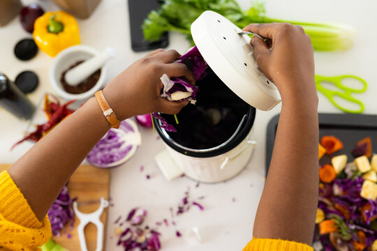 Hands of plus size african american woman composting vegetable waste in kitchen