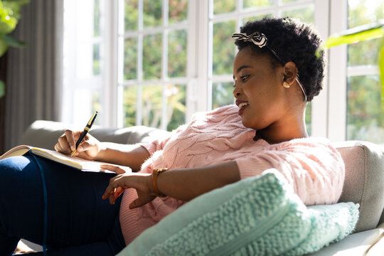 Happy Plus Size African American Woman Taking Notes In Notebook In Living Room