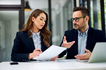 A businesswoman reading documents and talking with a male colleague at the office.