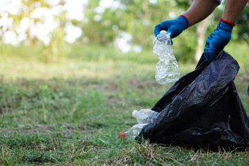 Close up hands are picking plastic bottles into black garbage bag in the park. Concept, keep clean...