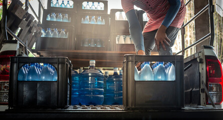 Workers lift blue drinking water bottles in crates into the back of a transport truck purified...